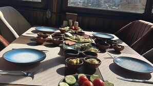 A dining table set with various dishes and bowls, a view of mountains through a window, and a chair. - Emit Sakura Cave Hotel (Nevsehir)