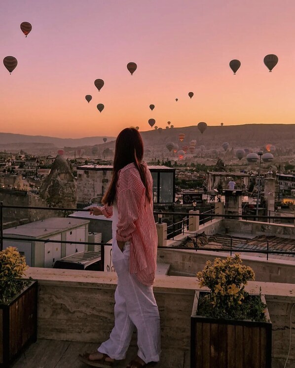 A person standing on a rooftop overlooking a cityscape with numerous hot air balloons in the sky. - Emit Cave Hotel (Nevsehir)
