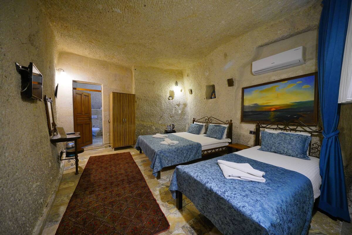 A room with two beds, a painting, an air conditioner, and a wooden door.