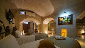 A hotel room with two beds, a TV, an air conditioning unit, a painting, and a small table with a lamp. - Emit Sakura Cave Hotel (Nevsehir)