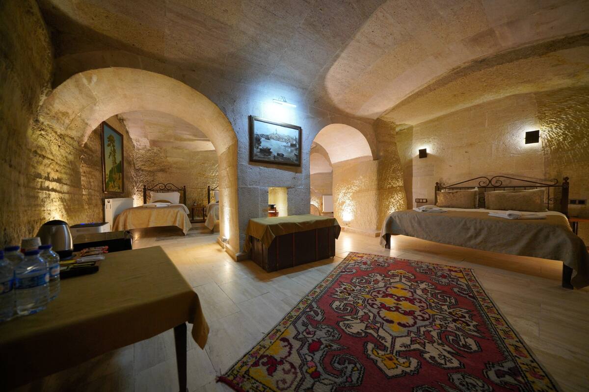 A rustic room with stone walls, a wooden table, a bed with a patterned rug, and a framed picture on the wall.