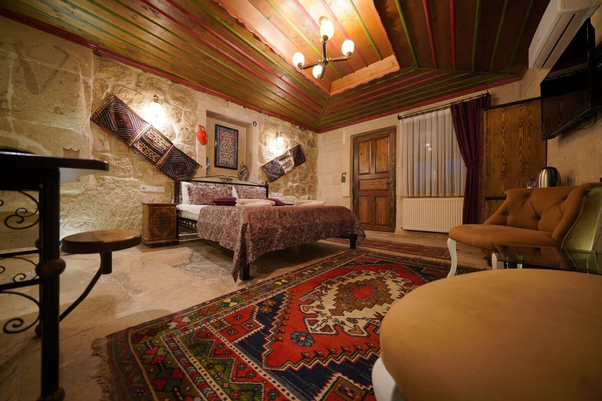 A bedroom with a bed, a wooden chair, a patterned rug, and a stone wall.
