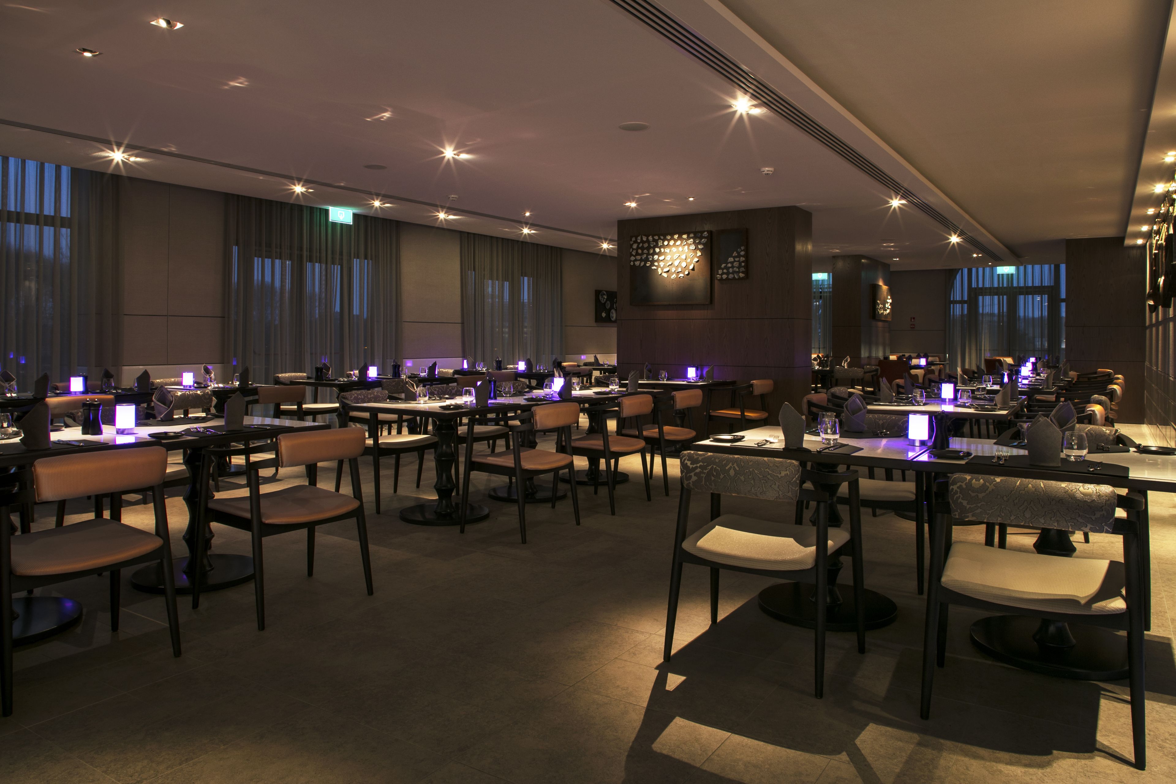A modern dining area with multiple tables and chairs, ambient lighting, and a contemporary interior design.