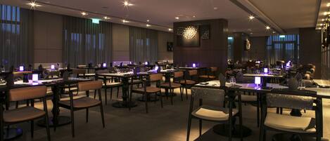 A modern dining area with multiple tables and chairs, ambient lighting, and a contemporary interior design.