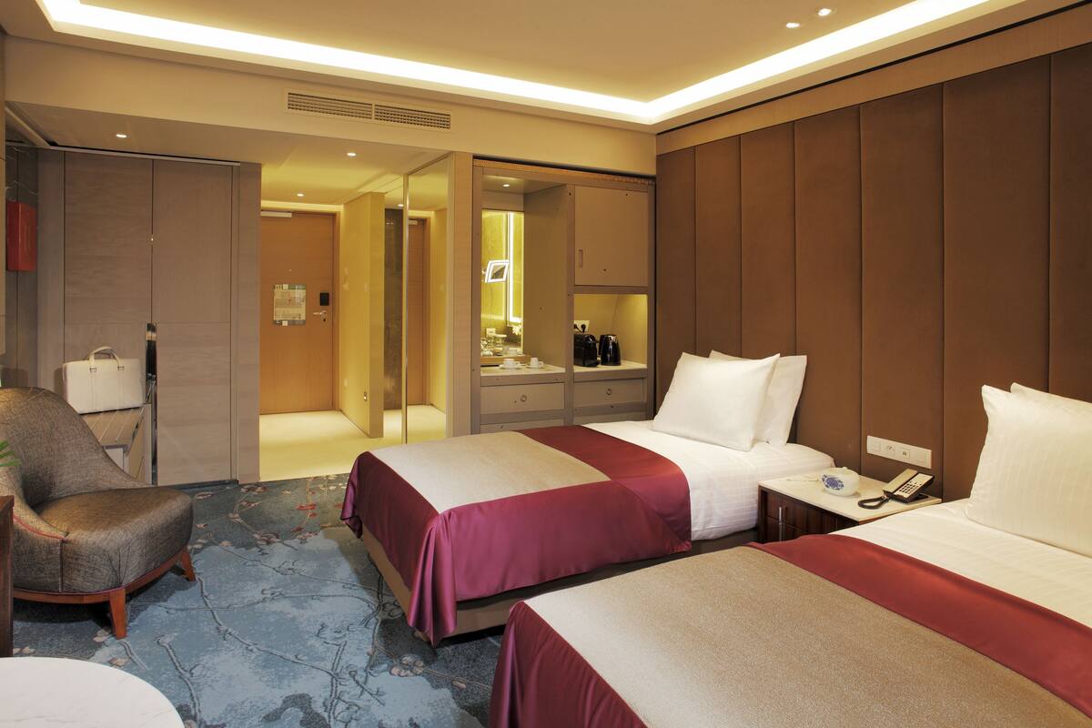 Habitación de hotel con dos camas, una silla, una mesita de noche y un espejo.
