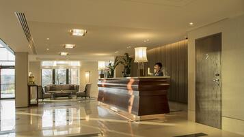 A modern hotel lobby with a reception desk, seating area, and large windows.
