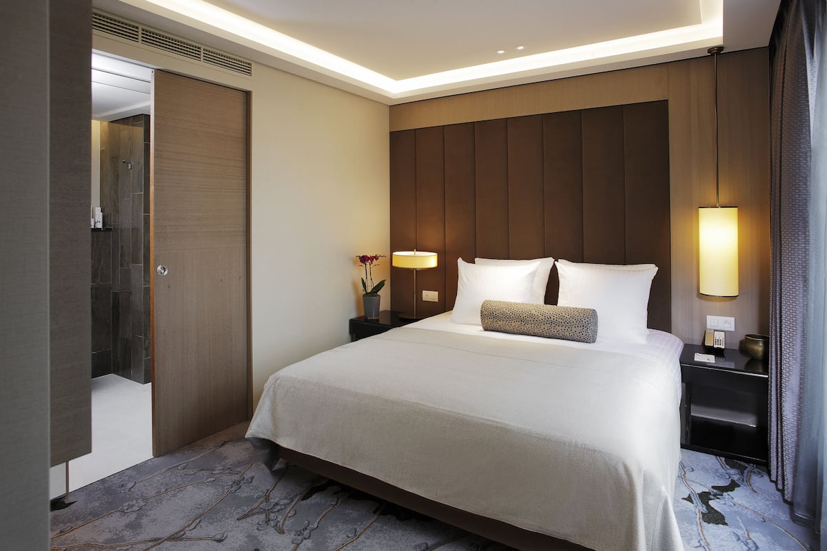 Habitación de hotel con una cama grande, una mesita de noche con lámpara, un atril y un armario.
