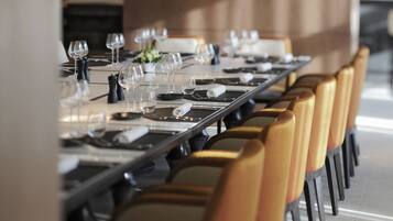 Una larga mesa de comedor dispuesta con múltiples sillas, cada una con base negra y cojín de color claro.