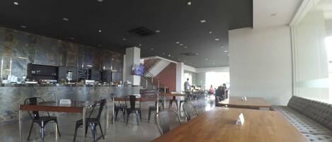 A modern restaurant with a bar area, seating arrangements, and a staircase leading to an upper level.