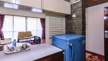 Uma cozinha compacta com geladeira azul, uma área de jantar com duas cadeiras, uma janela com cortinas e uma parede de pedra.
