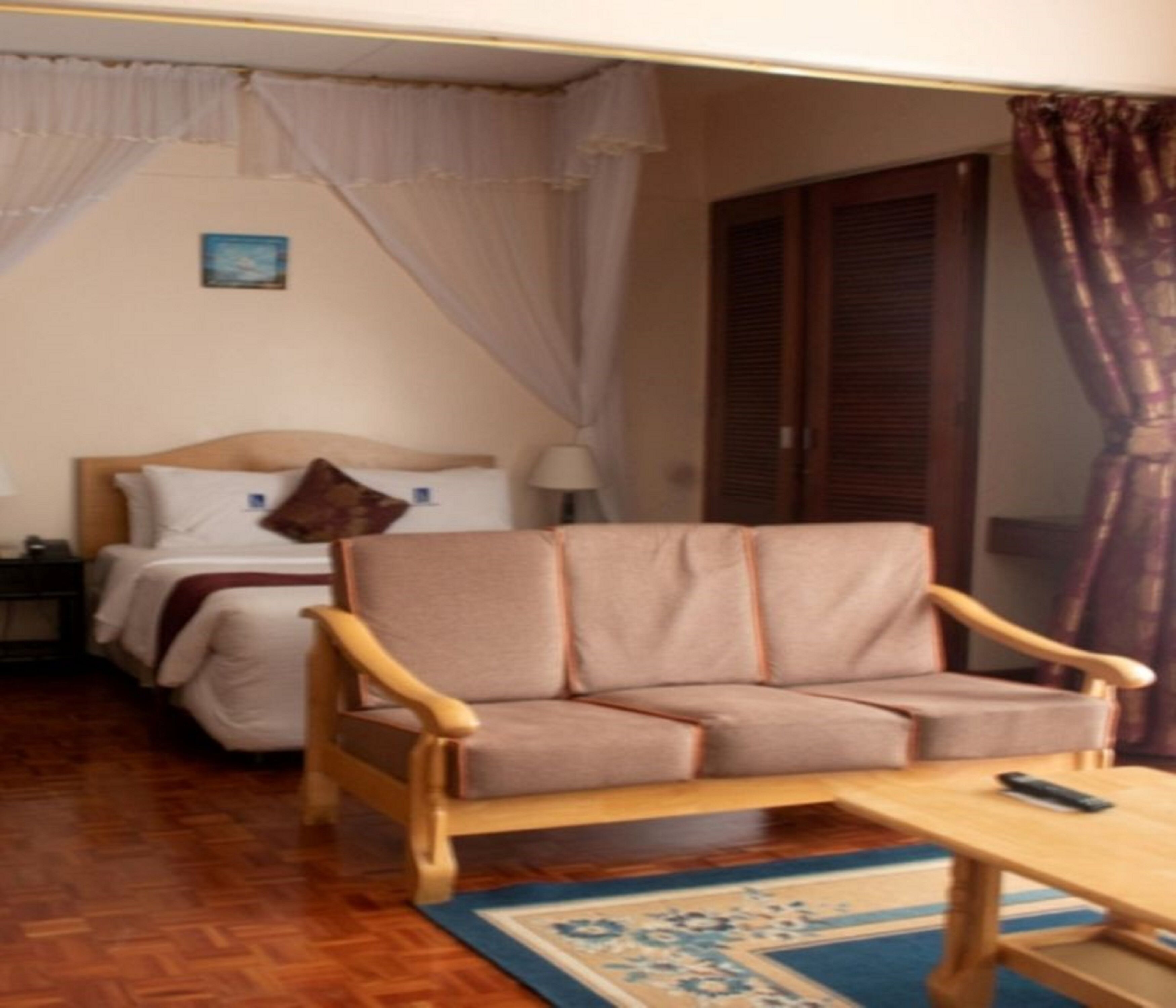 Habitación de hotel con una cama de madera, un sofá color beige, una mesa de centro de madera y una alfombra estampada.