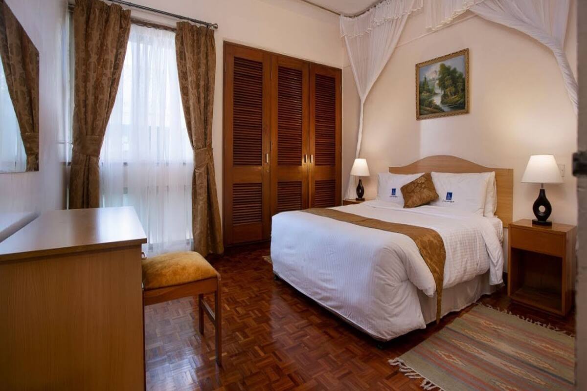 Habitación de hotel con cama, escritorio, silla, armario y un cuadro en la pared.