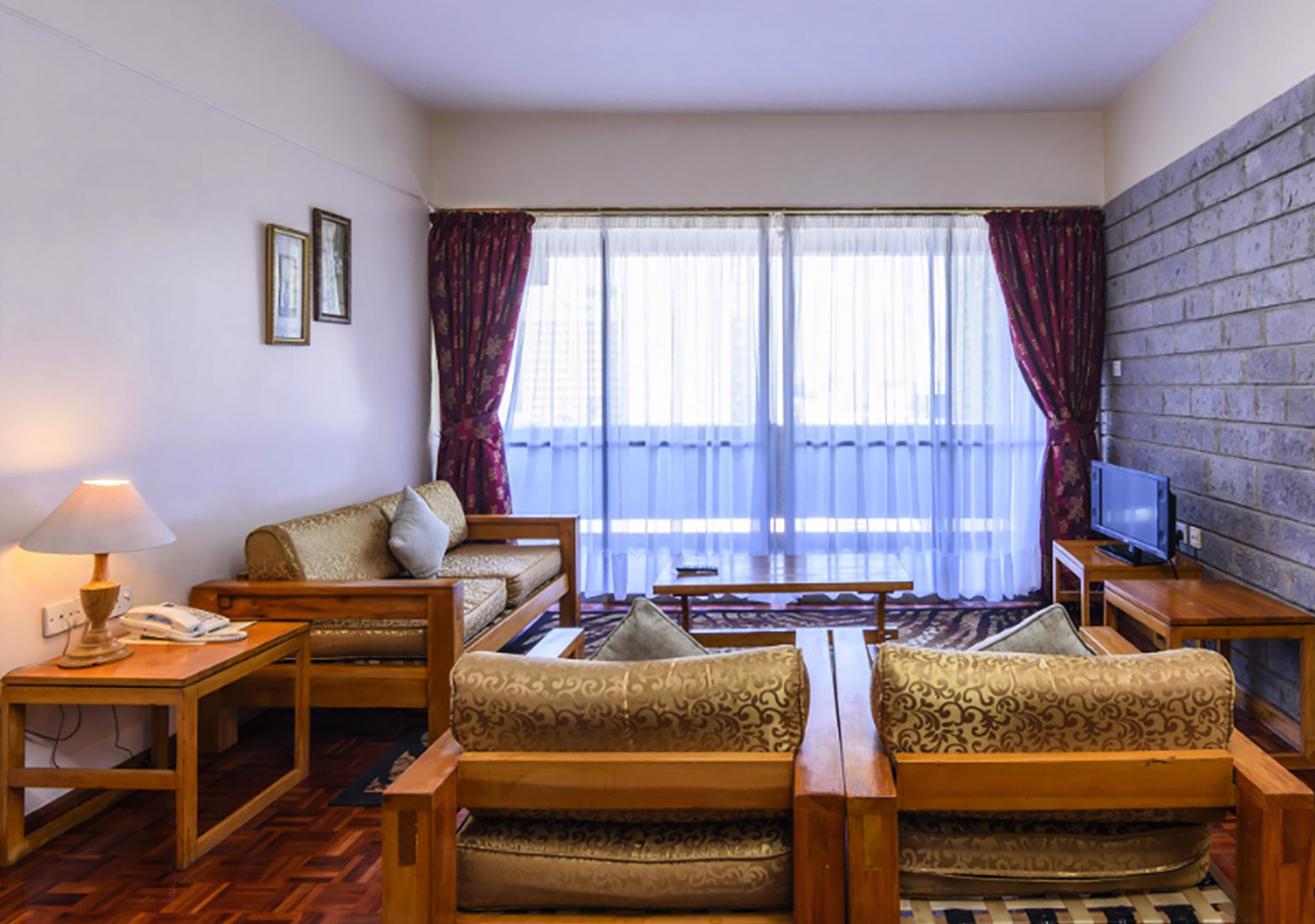 A hotel room with a sofa set, a television, a lamp, and a window with curtains.
