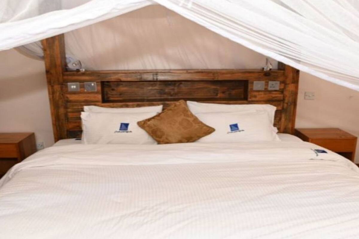 Una cama con cabecera de madera, ropa de cama blanca y almohada marrón.