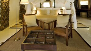 Une pièce avec un toit de chaume, un lit à baldaquin et une table basse en verre.