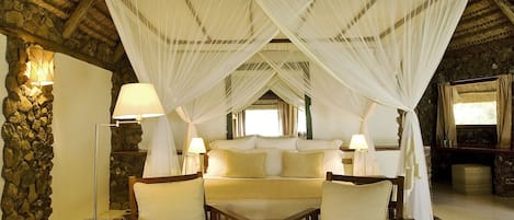 A room with a thatched roof, a bed with a canopy, and a glass coffee table.