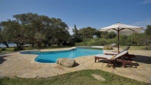 Une piscine entourée d’une terrasse en pierre, avec des chaises longues et un parasol.