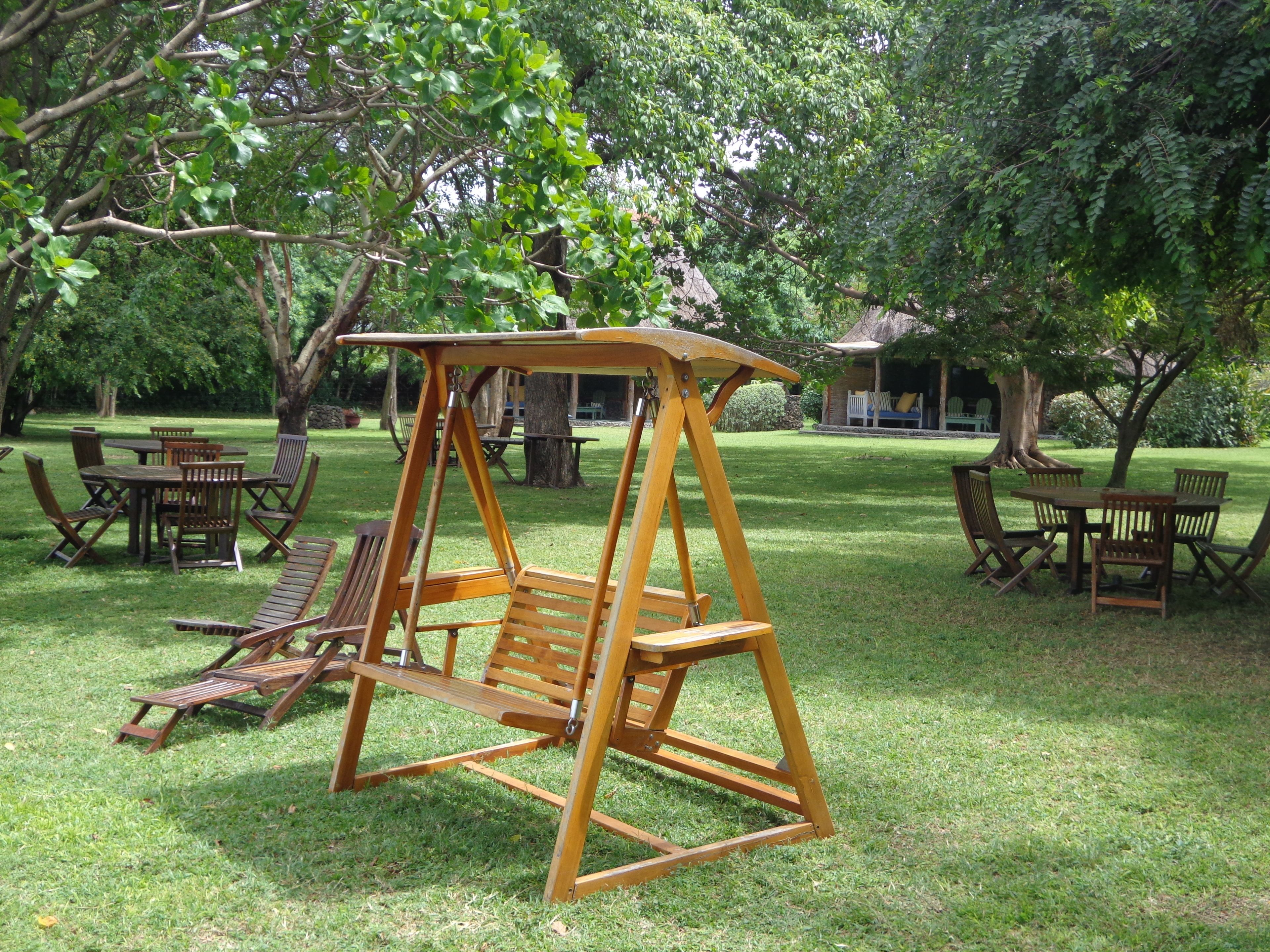 A wooden swing set in a grassy outdoor area with picnic tables and chairs.