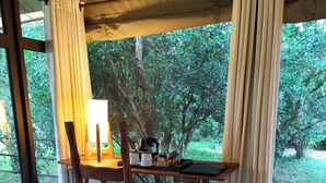 A wooden table with chairs, a lamp, and a laptop in a room with large windows and curtains. - Ashnil Mara Camp (Maasai Mara)