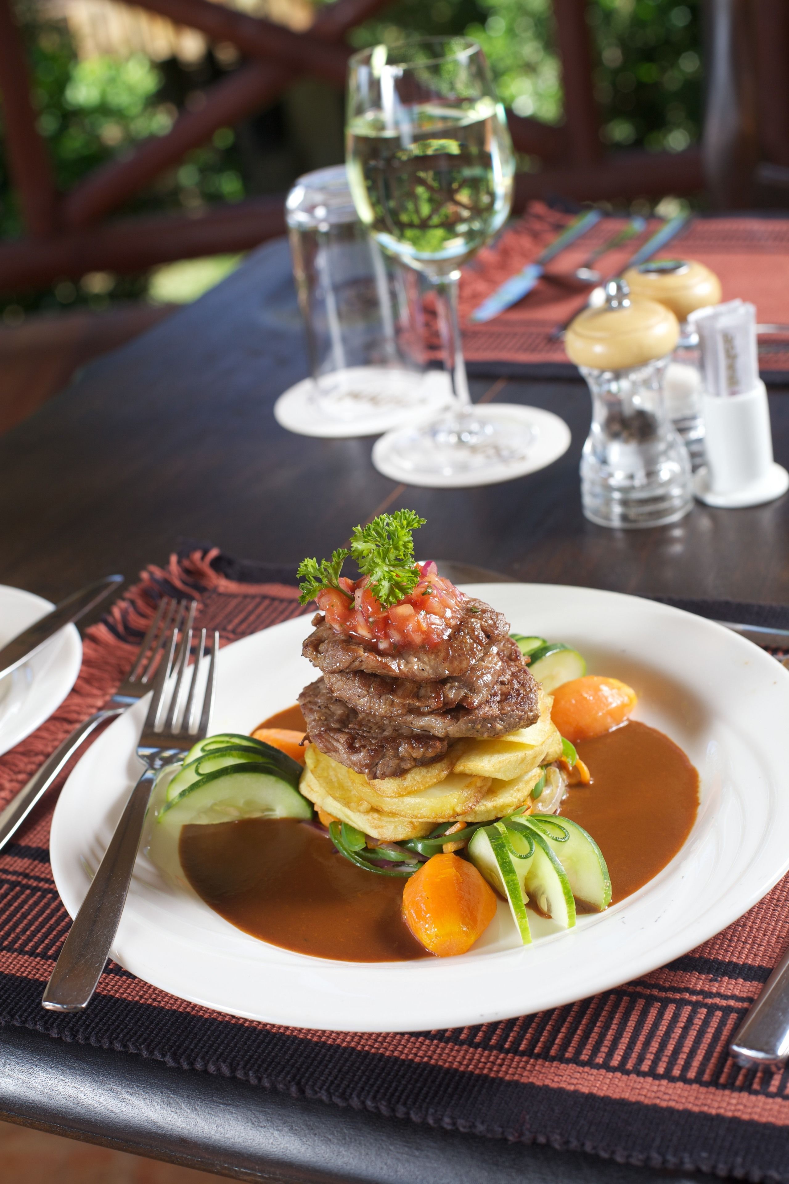 Een bord met eten, inclusief een steak, groenten en saus, op een tafel met een placemat.