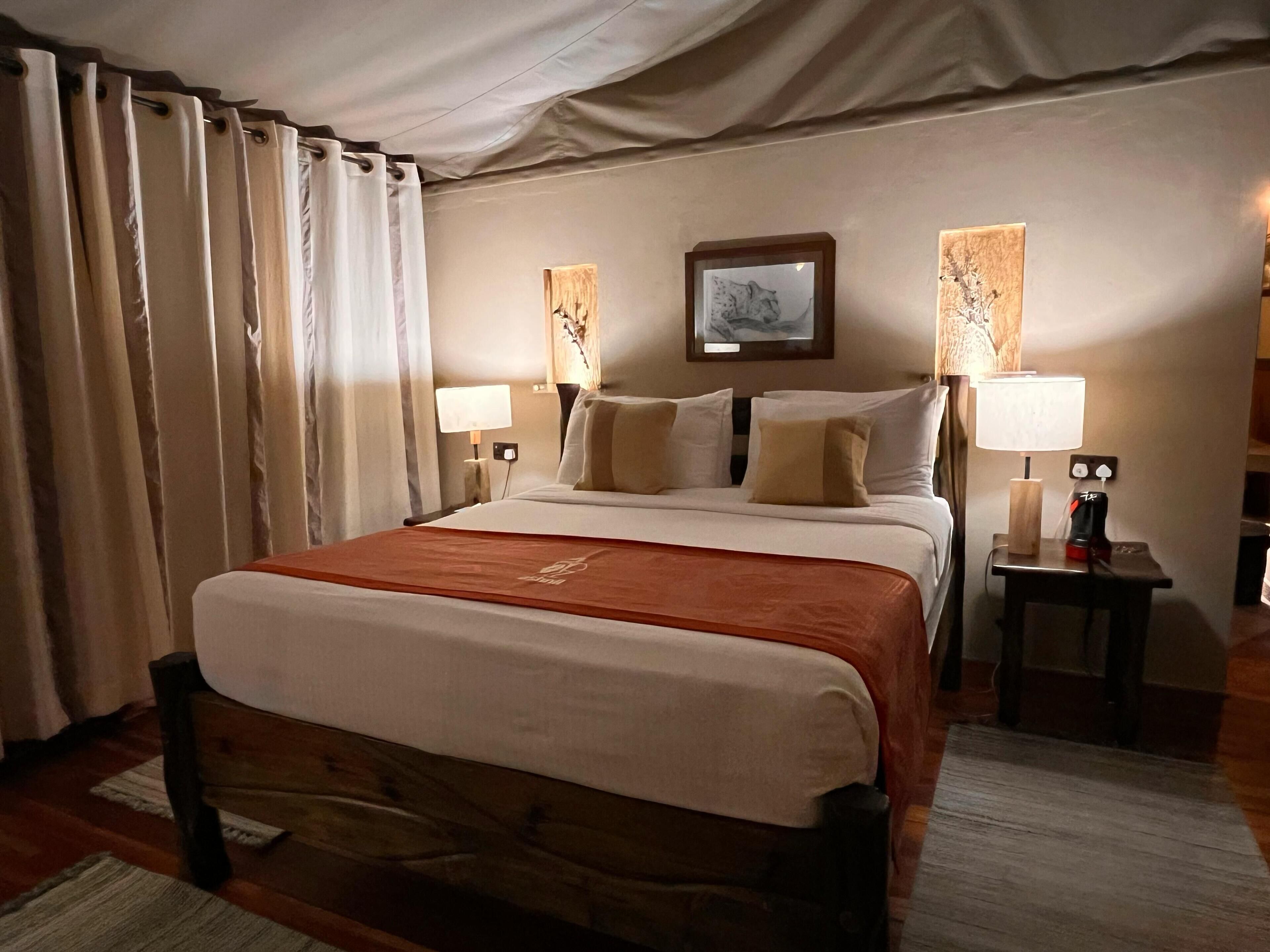 A hotel room with a large bed, two bedside tables, a nightstand, a lamp, and a framed picture on the wall.