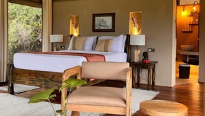 A bedroom with a large bed, two bedside lamps, a wooden chair, and a view of greenery outside. - Ashnil Mara Camp (Maasai Mara)