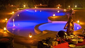 A poolside dining area with a table set for a meal, surrounded by candles and a large metal bowl. - Ashnil Mara Camp (Maasai Mara)