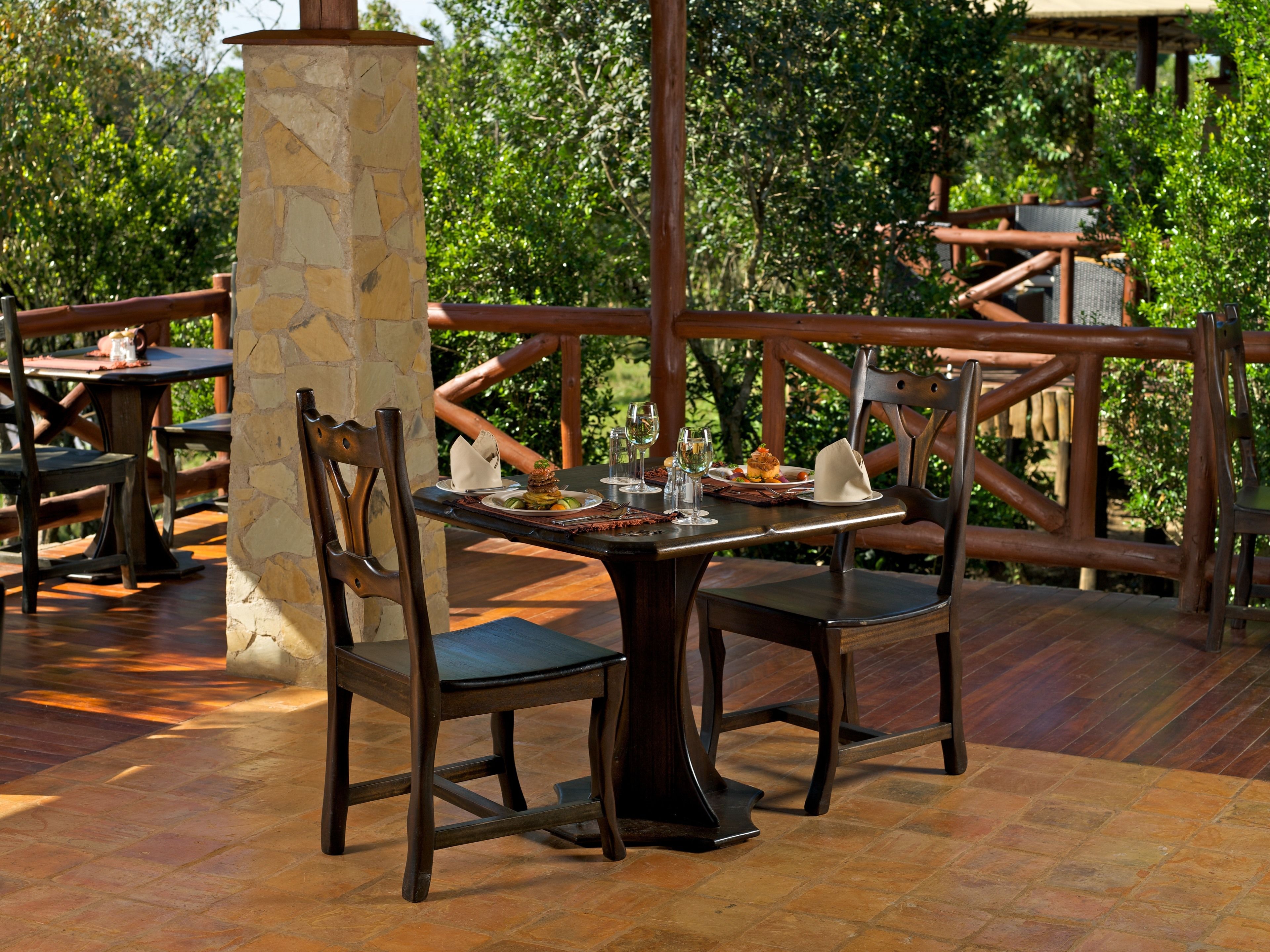 An outdoor dining area with stone pillars, wooden chairs, and tables.