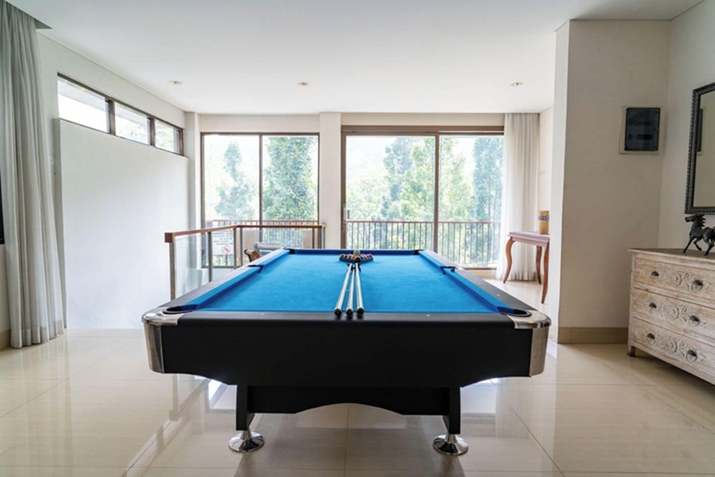 A pool table in a room with large windows, a balcony, and a dresser.