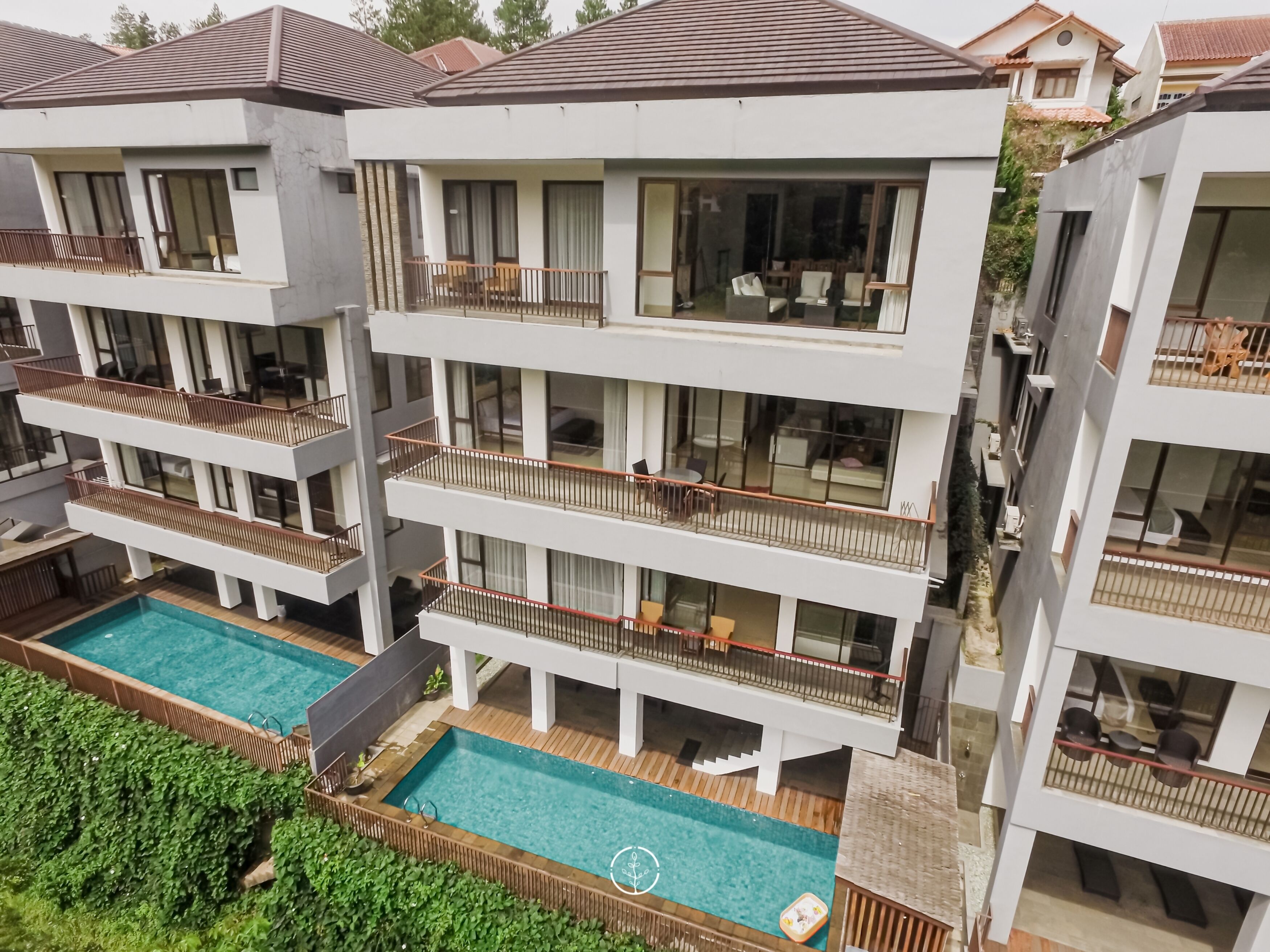 Um edifício residencial com vários andares, varandas, piscina e vista para casas vizinhas.