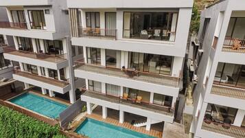 Um edifício residencial com vários andares, varandas, piscina e vista para casas vizinhas.