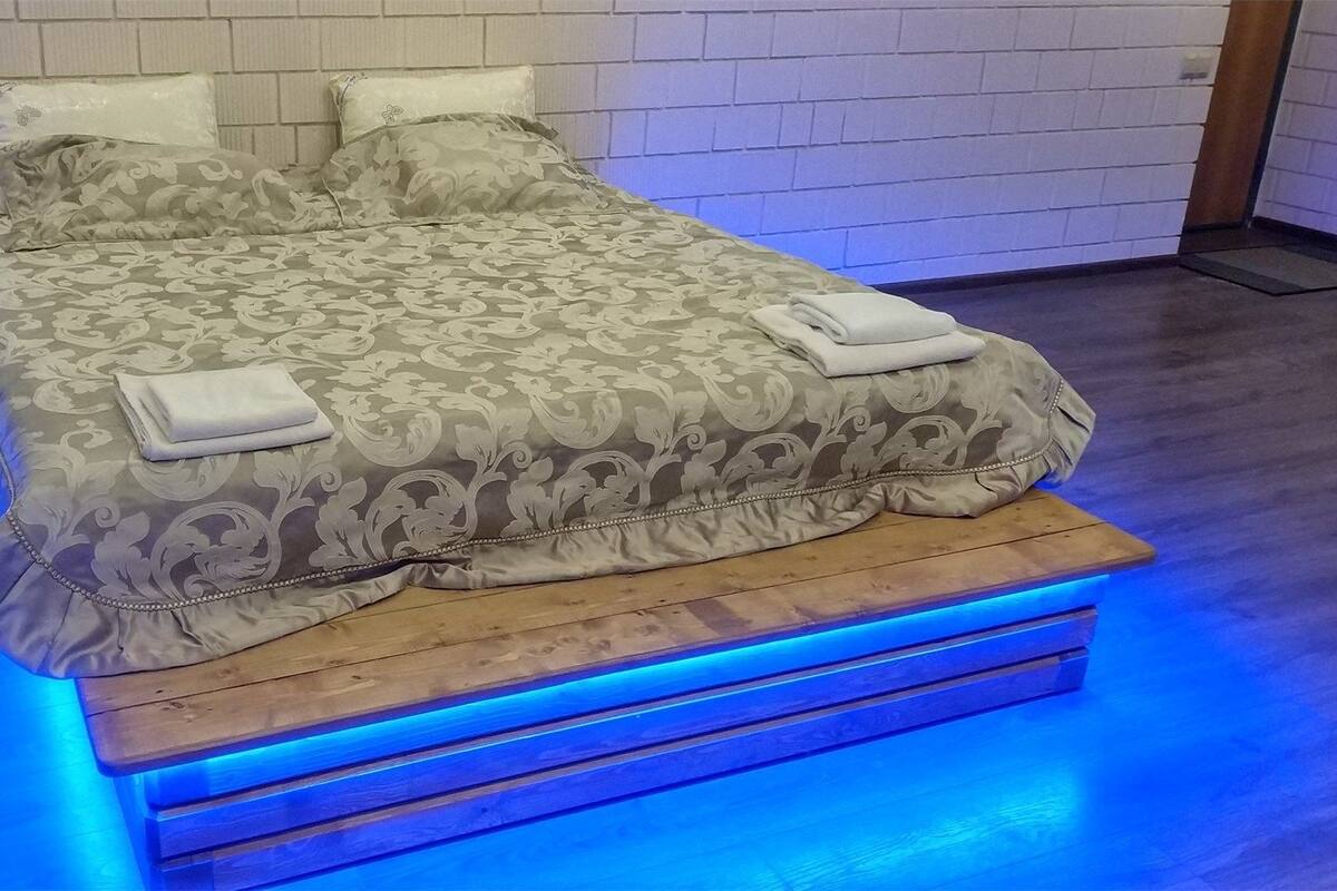 Un lit avec une couvre-lit à motifs et des oreillers, une plateforme en bois et un éclairage d’ambiance bleu.