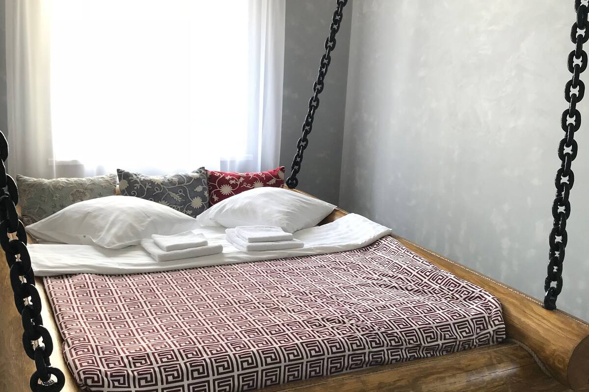 Un lit avec une couvre-lit à motifs géométriques, des oreillers blancs et une tête de lit en bois ornée de chaînes.