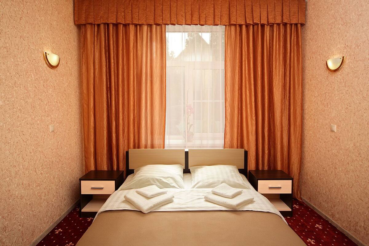 Une chambre d’hôtel comprenant un lit, deux tables de chevet, une fenêtre avec des rideaux et des appliques murales.