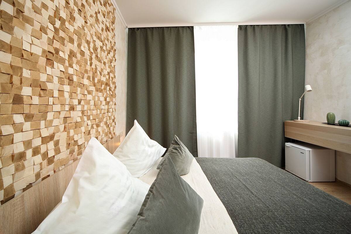 Une chambre moderne avec un mur en bois, un lit avec des oreillers, une table de chevet, une lampe et un petit cactus.
