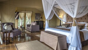 Une chambre spacieuse avec un grand lit, un coin salon avec une chaise et une table, et une structure de plafond en forme de tente.