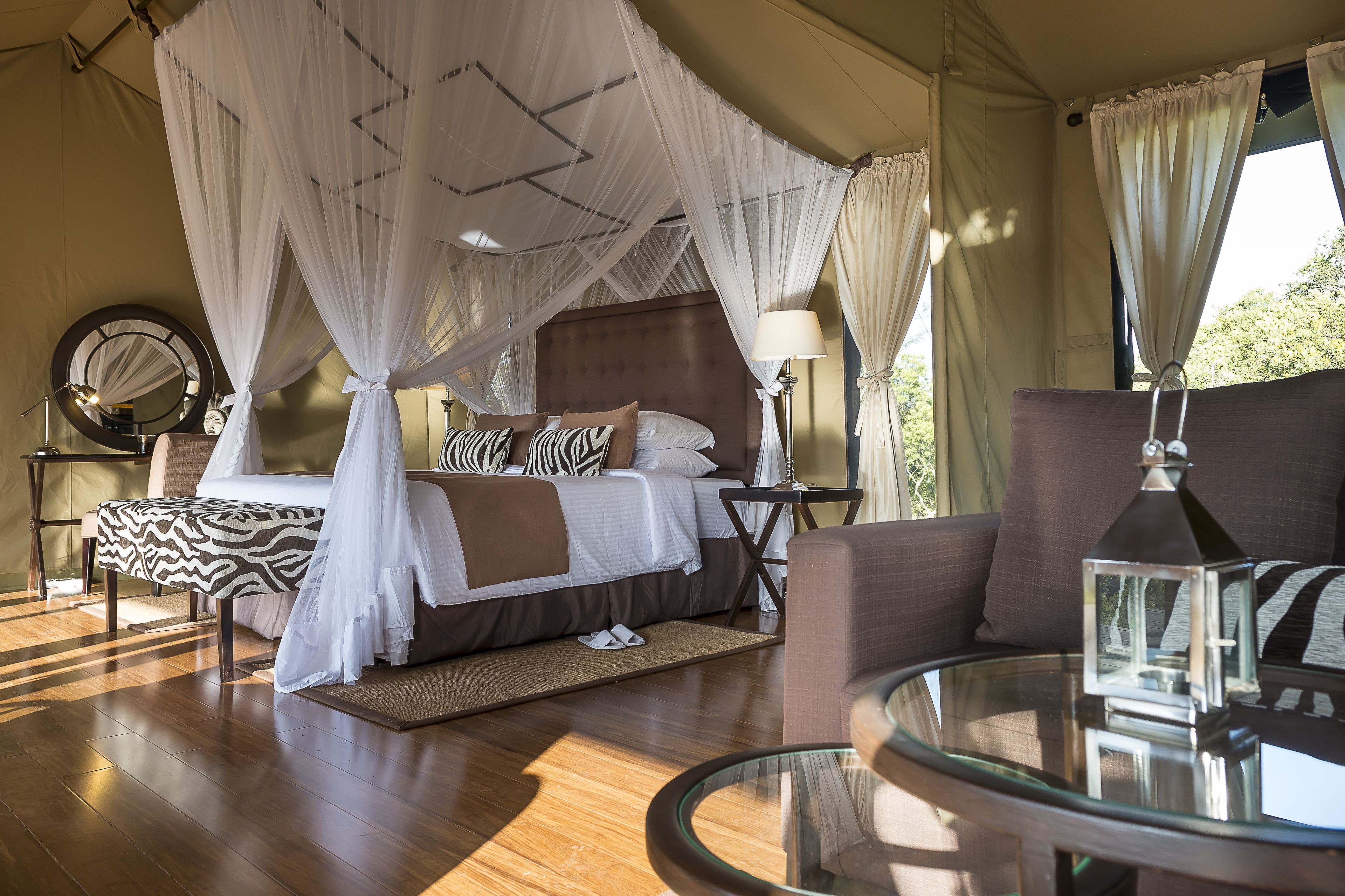 A bedroom with a canopy bed, a round glass table, and a nightstand with a lamp.