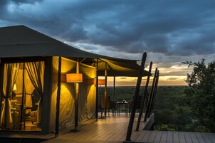 A tented accommodation with a wooden deck, a dining area, and a view of the landscape.