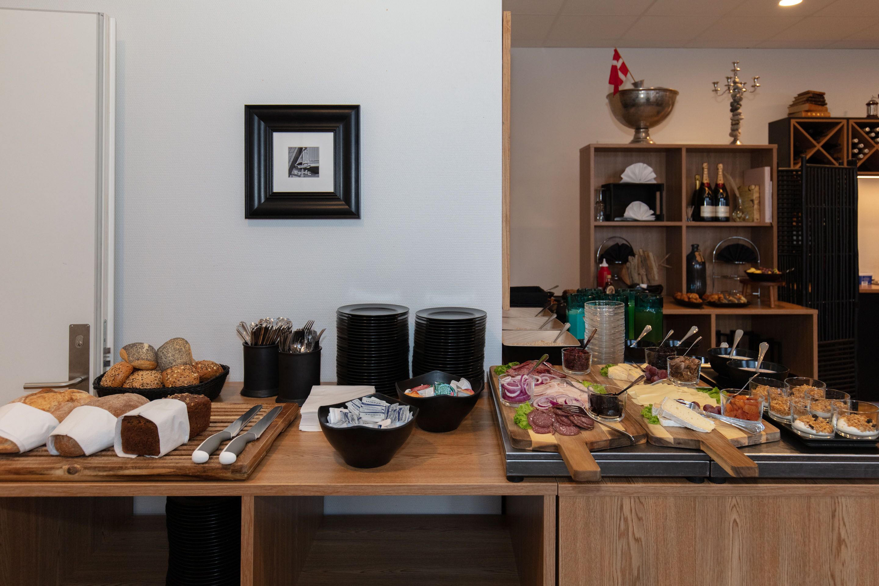 Ein reichhaltiges Buffet mit verschiedenen Speisen, darunter Brot, Käse und Wurst, sowie Geschirr und Besteck.