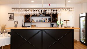 Un espace bar avec un comptoir en bois, des étagères remplies de bouteilles et un réfrigérateur.