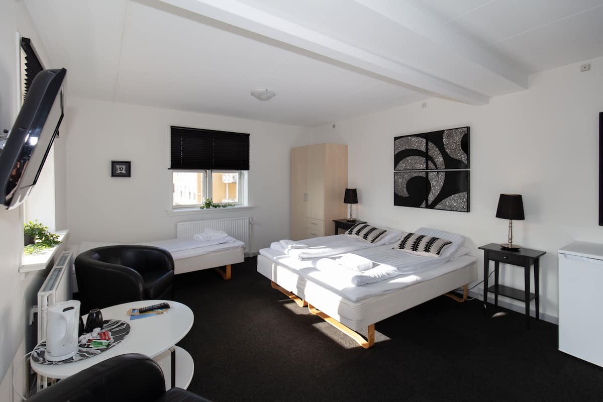Una habitación de hotel moderna con cama, escritorio, silla, mesita, televisor y ventana con persianas.