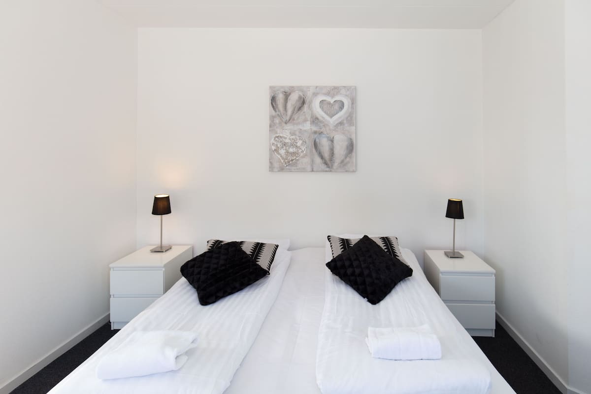 Habitación de hotel con dos camas, ropa de cama blanca, almohadas negras, una obra de arte en la pared y lámparas de noche.