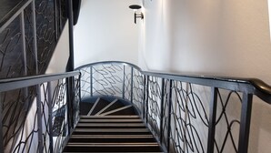 Un escalier avec une rampe en métal, un luminaire fixé au mur et une porte portant un numéro.