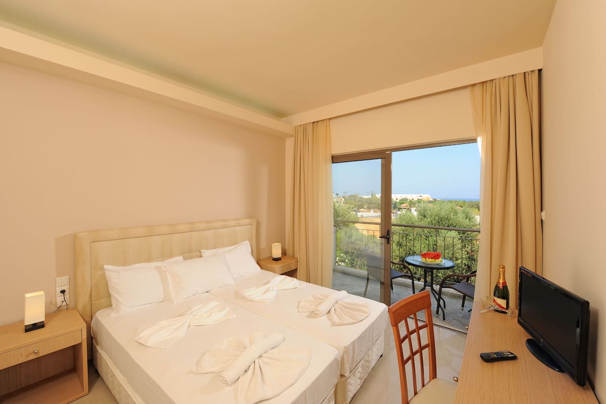Habitación de hotel con cama, televisor, control remoto y balcón con mesa y silla.