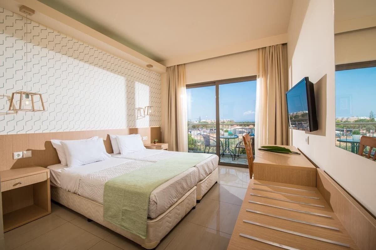Habitación de hotel con una cama grande, un escritorio, un televisor y un balcón con vista a la ciudad.