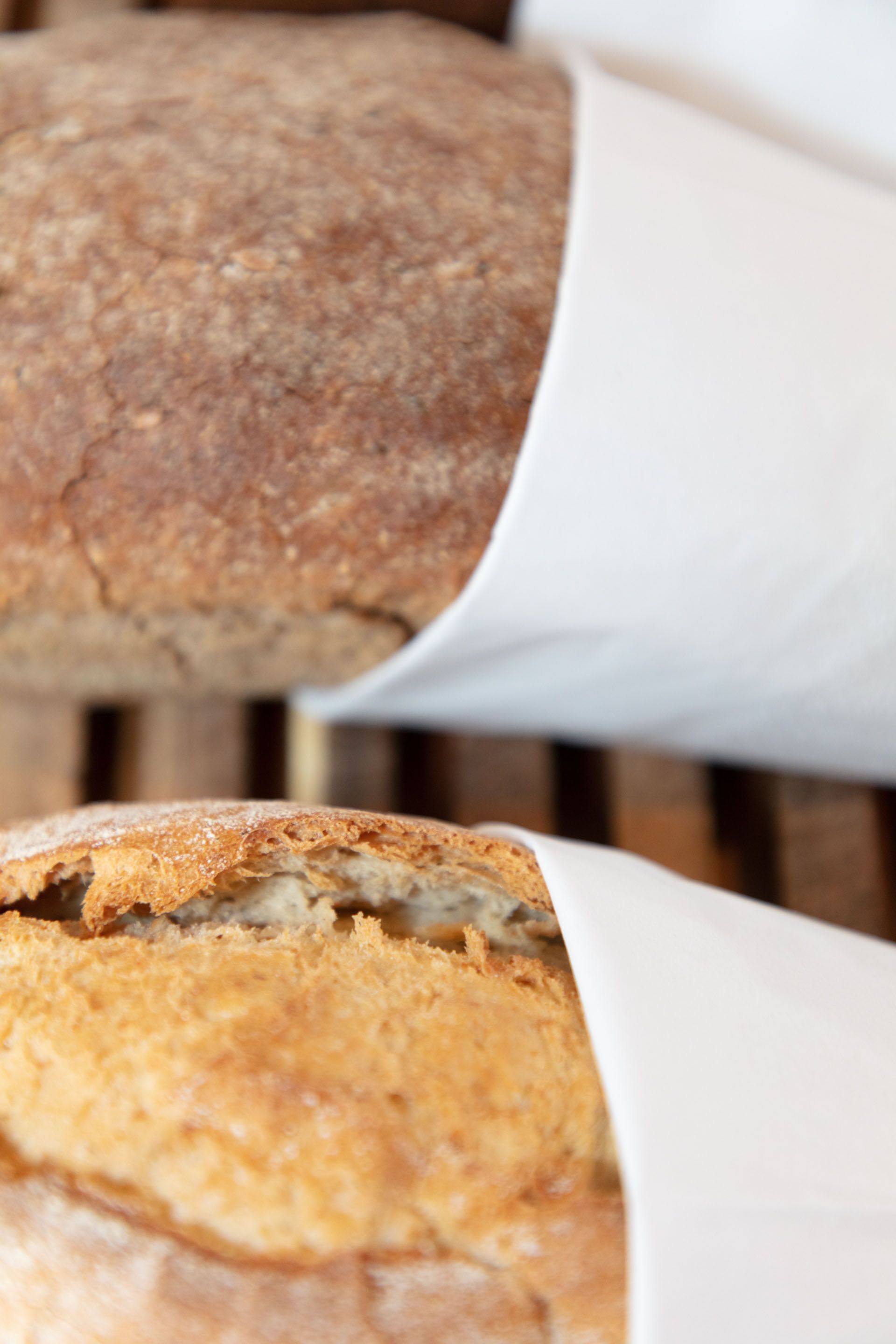 A loaf of bread with a crusty exterior and a soft interior, partially wrapped in white paper.