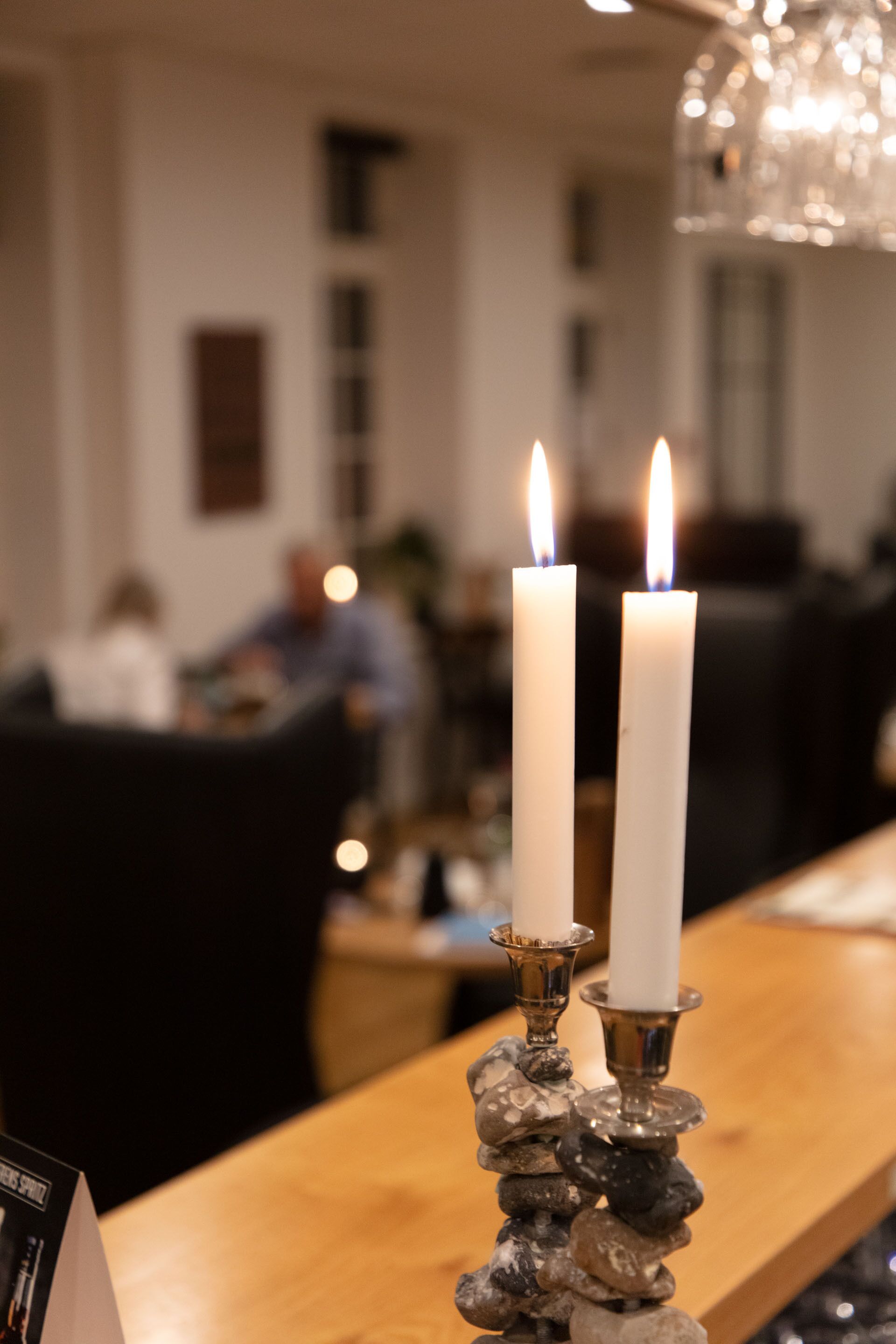 Two lit candles on a wooden table with a decorative rock holder.