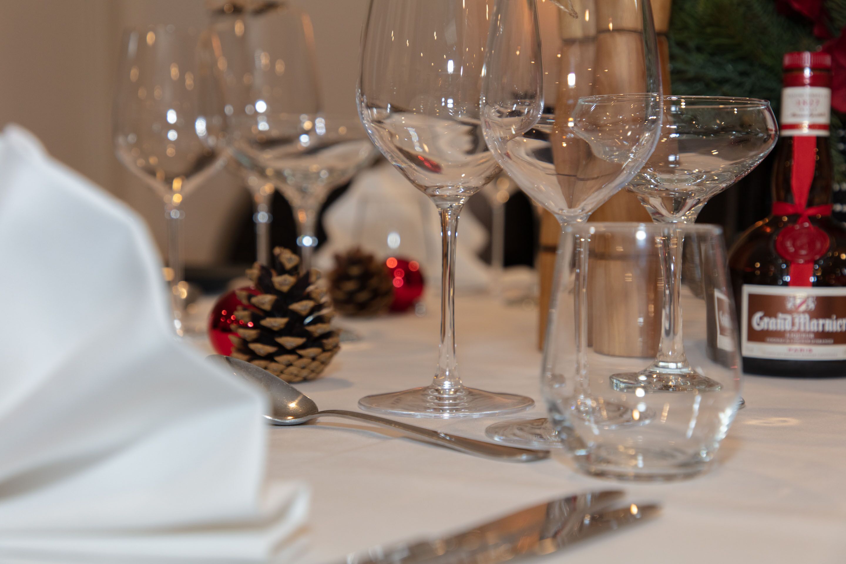A table set with wine glasses, a bottle of wine, and a pine cone decoration.