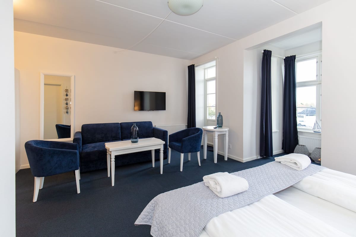 Habitación de hotel con cama, dos sillas, una mesita, televisor y ventana con cortinas.