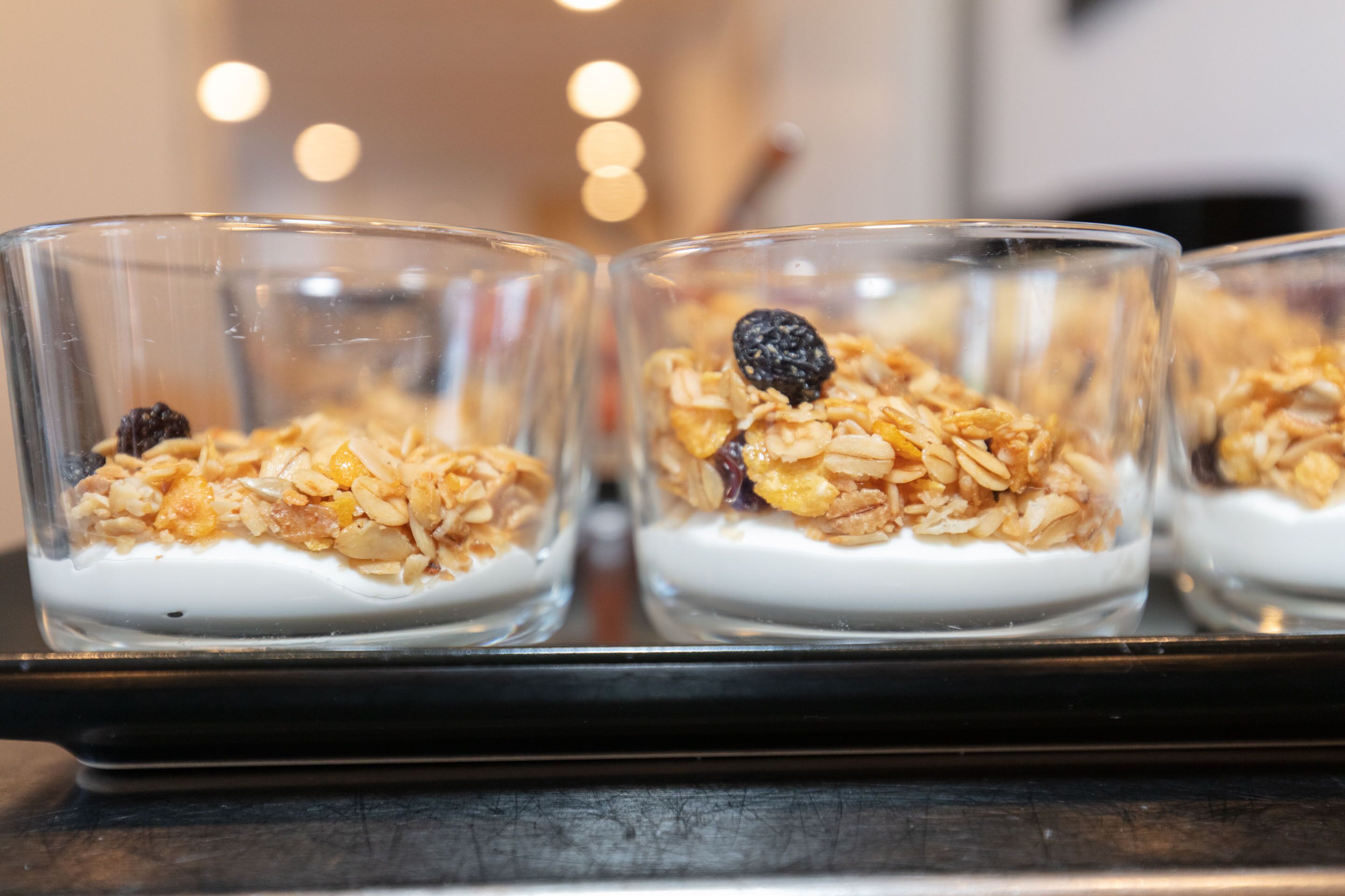 Four glass bowls of yogurt topped with granola and dried fruit on a tray.
